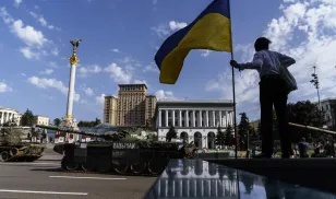 A woman holds the flag of Ukraine while looking over a row of destroyed Russian military vehicles on display at Maidan Square in Kyiv, Ukraine