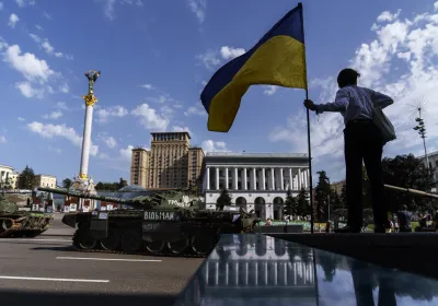 A woman holds the flag of Ukraine while looking over a row of destroyed Russian military vehicles on display at Maidan Square in Kyiv, Ukraine