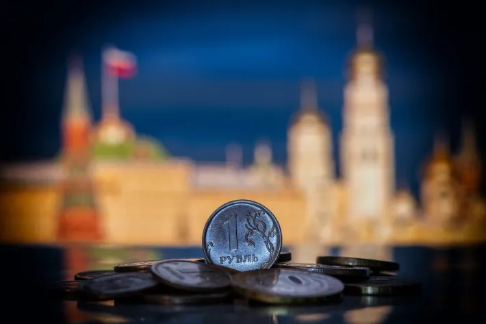 Coin in denomination of 1 Russian ruble on a pile of other coins in front of symbolic out-of-focus fragments of the Moscow Kremlin 